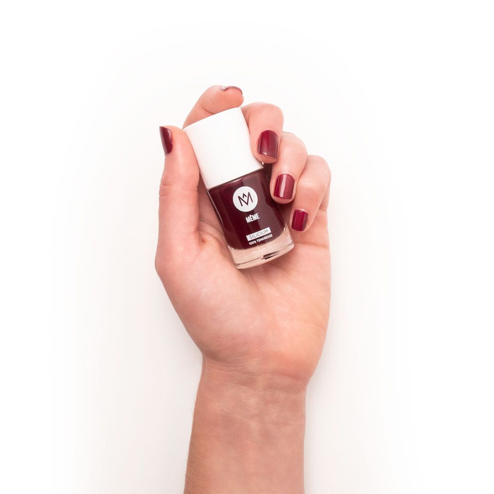Hand hält eine Nagellackflasche. Auf dem Nagel ist Nagellack. Auf der Flasche steht MEME und SILICIUM. Die Farbe ist dunkelrot.