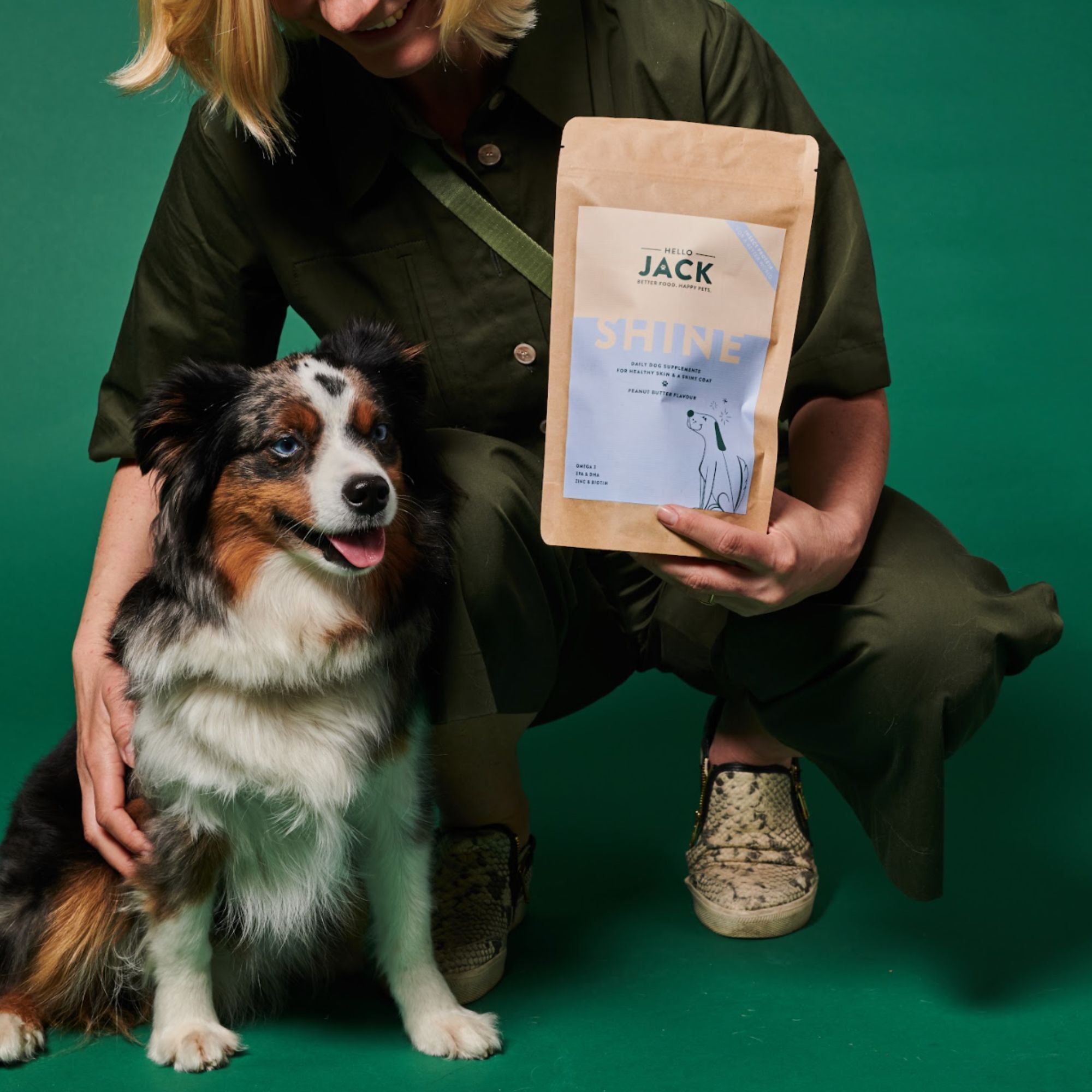 Frau hält Beutel "Hello Jack Shine" neben Hund. Hund sitzt. Erdnussbutter-Geschmack.