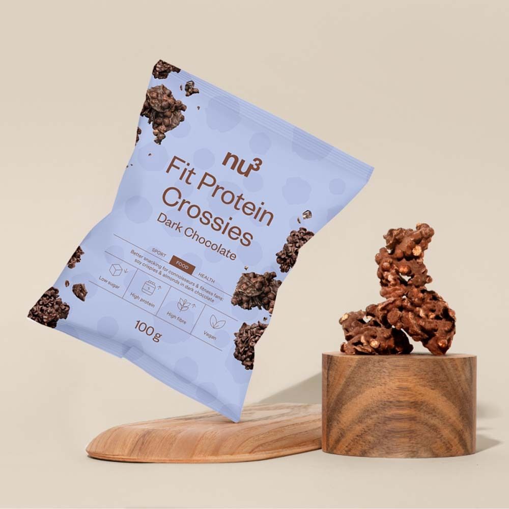 Produktverpackung von nu3 Fit Protein Crossies, dunkle Schokolade, auf einem Holzsockel. Daneben ein Holzbrett.