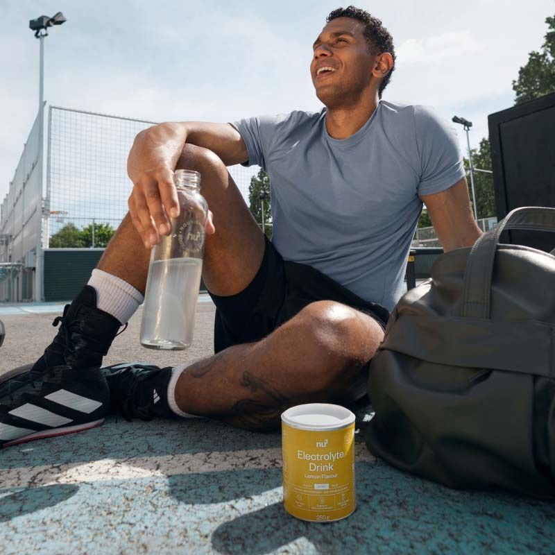Mann sitzt nach dem Sport neben Nu3 Elektrolyte Drink Dose und Wasserflasche.