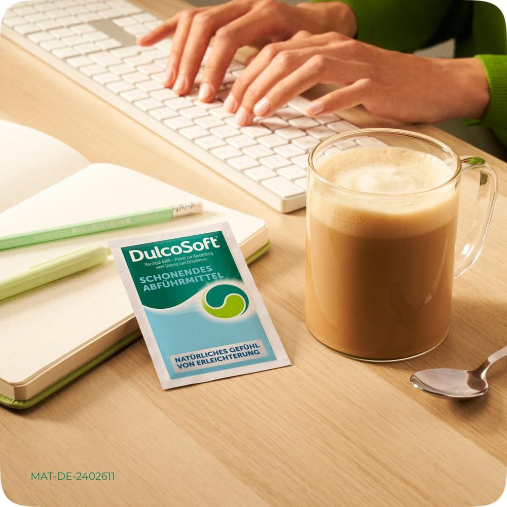 Person am Schreibtisch mit Kaffee und DulcoSoft-Beutel. Text: Natürliches Gefühl von Erleichterung.
