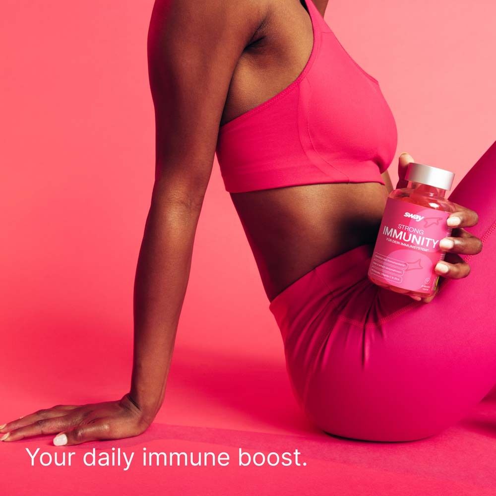 Person hält eine Flasche STRONG IMMUNITY. Person trägt Sport-BH und Leggings. Hintergrund pink.