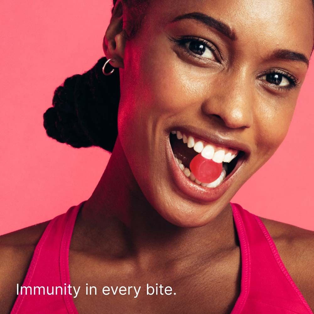 Person öffnet Mund mit rotem Gummibärchen. Hintergrund pink.