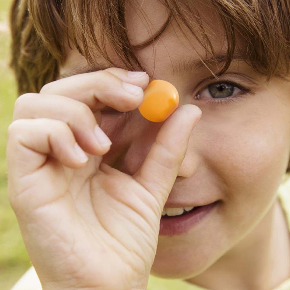 Ein Kind hält eine orangefarbene Jelly in der Hand vor seinem Auge. Das Kind lächelt.