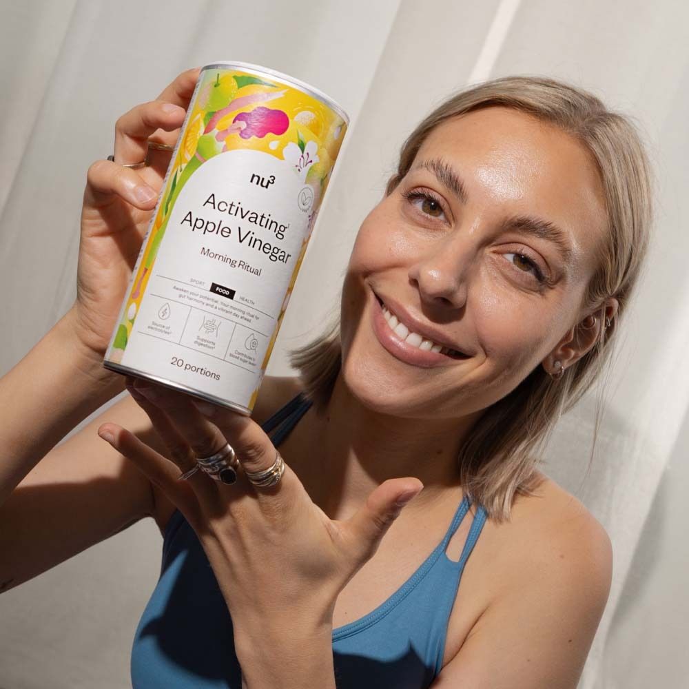 Frau hält Dose "nu3 Activating Apple Vinegar". Produktname und Logo sichtbar. Frau lächelt.