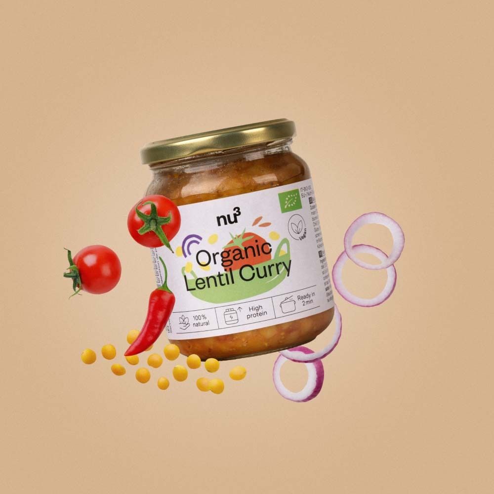 Glas mit nu3 Organic Linsen-Curry, umgeben von Tomaten, Chili, Zwiebelringen und Linsen. Produkt- und Zutaten-Arrangement auf beigem Hintergrund.