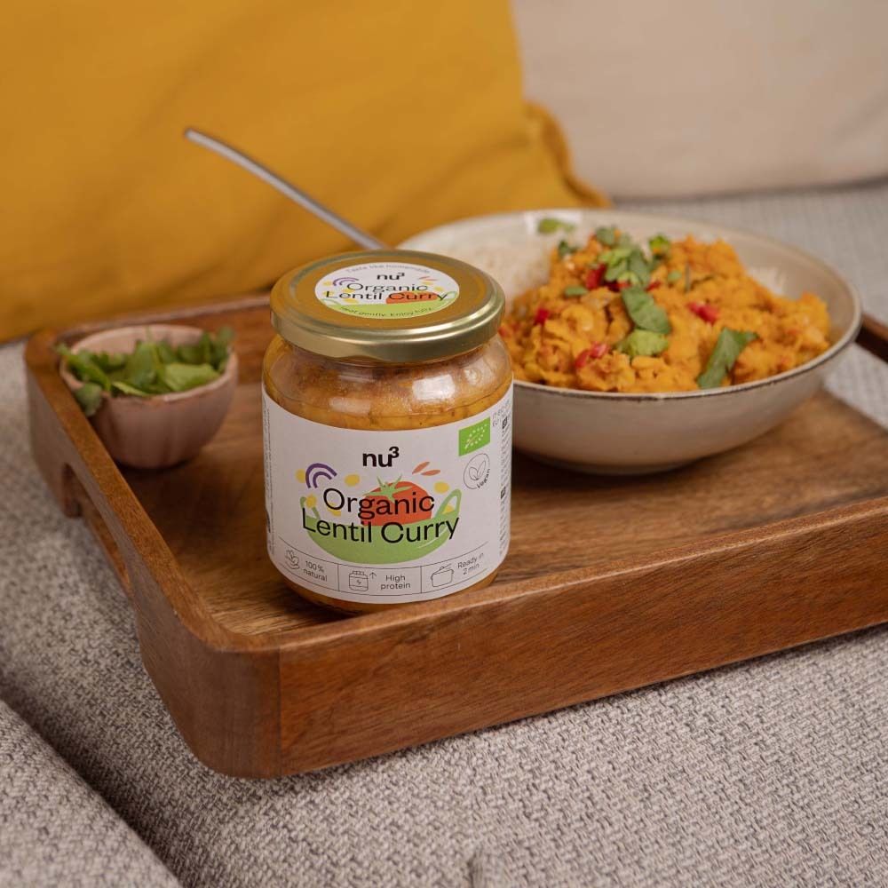 Glas mit nu3 Organic Linsen-Curry auf einem Holztablett. Daneben eine Schale mit Minze und eine Schüssel mit Reis und Curry.