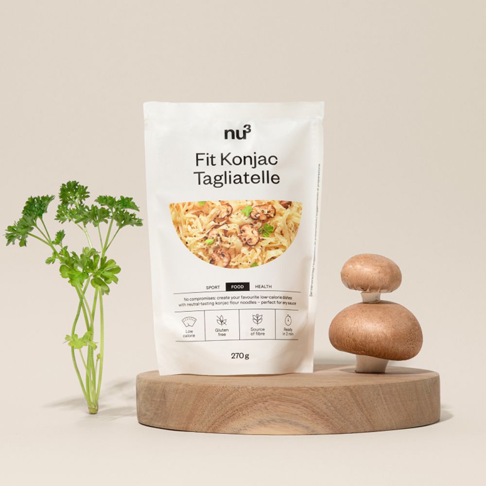 Eine Packung nu3 Fit Konjak-Tagliatelle auf einem Holzbrett mit Pilzen und Petersilie.