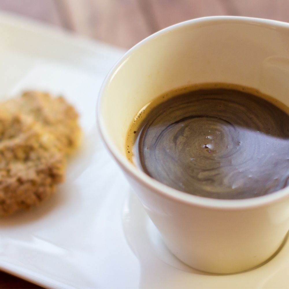 Eine Tasse Kaffee mit einem Keks auf einem weißen Teller.