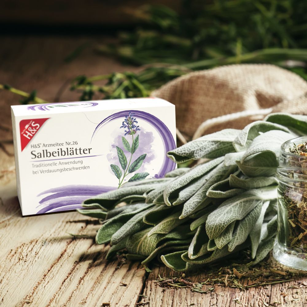 H&S Salbeiblätter Nr. 26 Packung neben Salbeiblättern und Kräutern. Holzuntergrund.