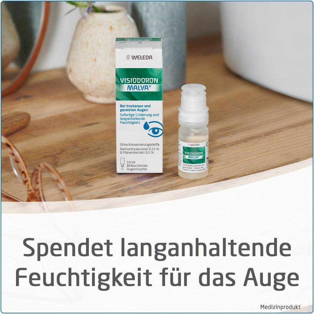 Eine Packung Visiodoron Malva Augentropfen von Weleda steht auf einem Holzregal neben einem Spiegel und einer Brille. Text: Spendet langanhaltende Feuchtigkeit für das Auge.