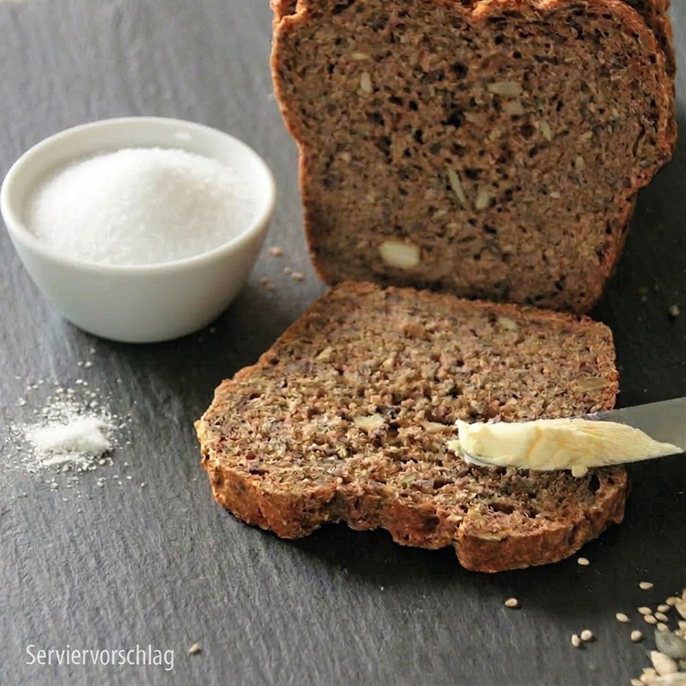 Brotlaib mit Scheiben, Butter und Salz auf dunklem Untergrund.