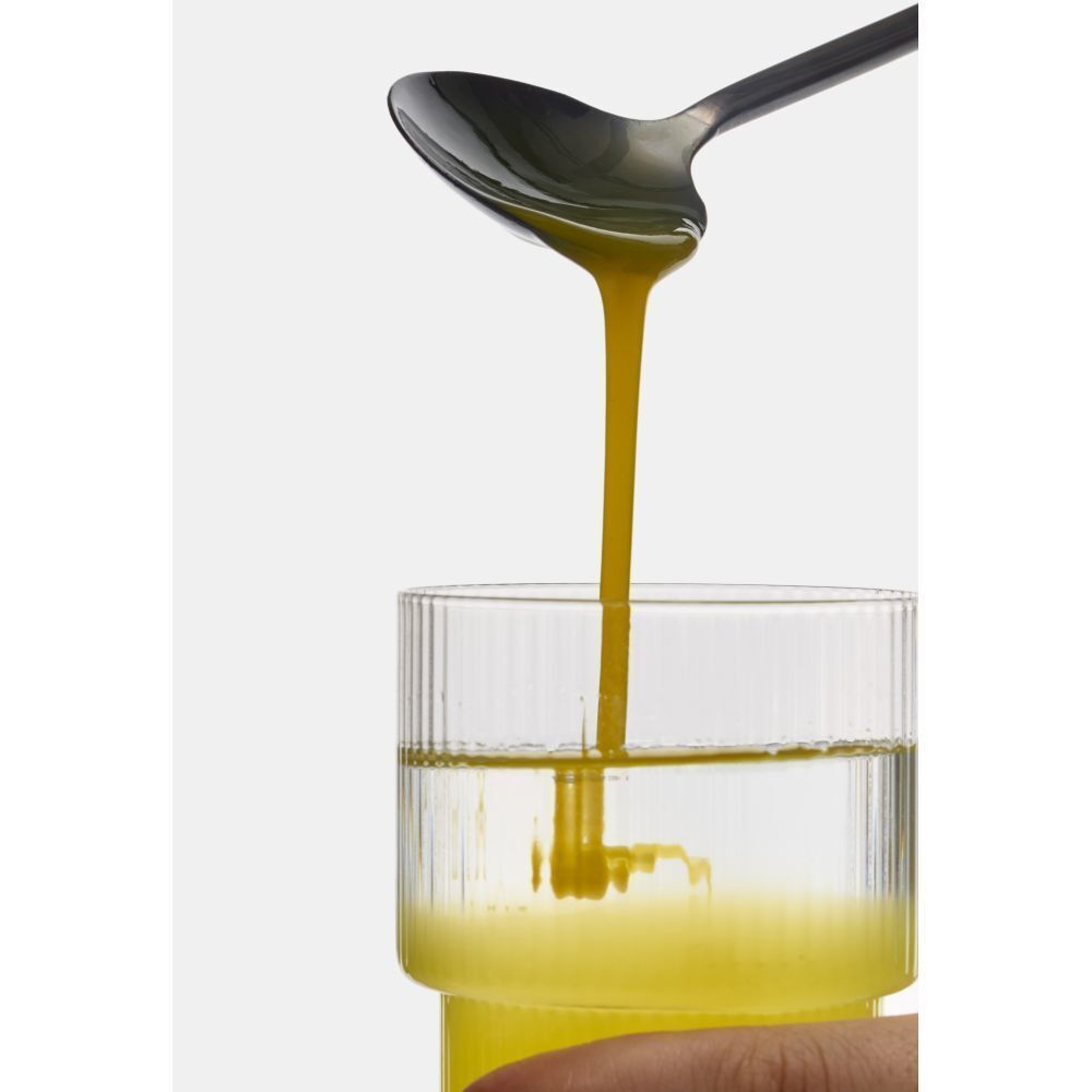 Gelbe Flüssigkeit wird aus einem Löffel in ein Glas mit Wasser gegossen.
