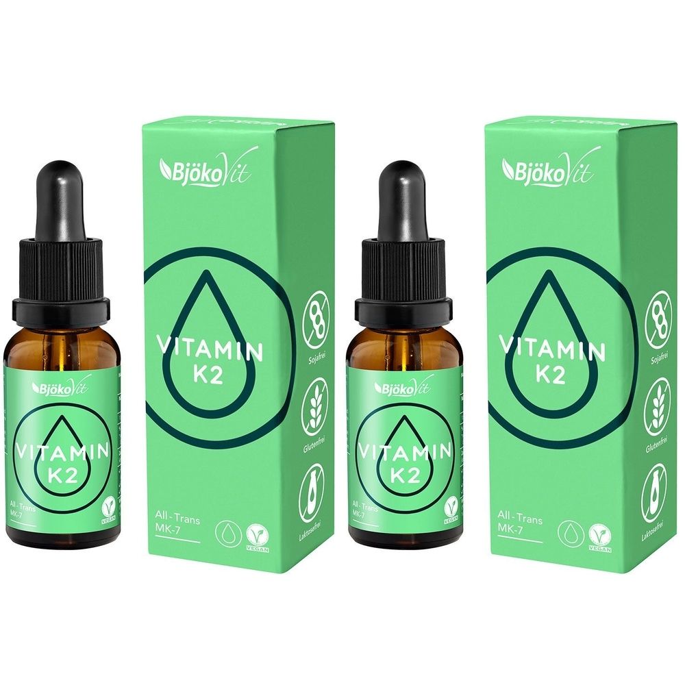 Braune Glasflaschen mit Tropfer und grüne Verpackungen. Aufschrift: Vitamin K2. Marke: BjökoVit. Tropfenflaschen und Verpackungen stehen nebeneinander.