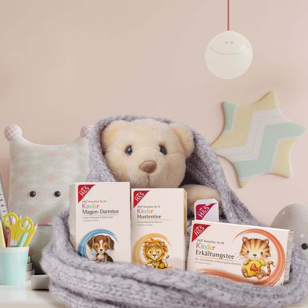 Drei Packungen Tee, darunter H&S® Kinder Magen-Darmtee. Abgebildet: Teddybär, Kuscheltiere. Hintergrund: rosa Wand.