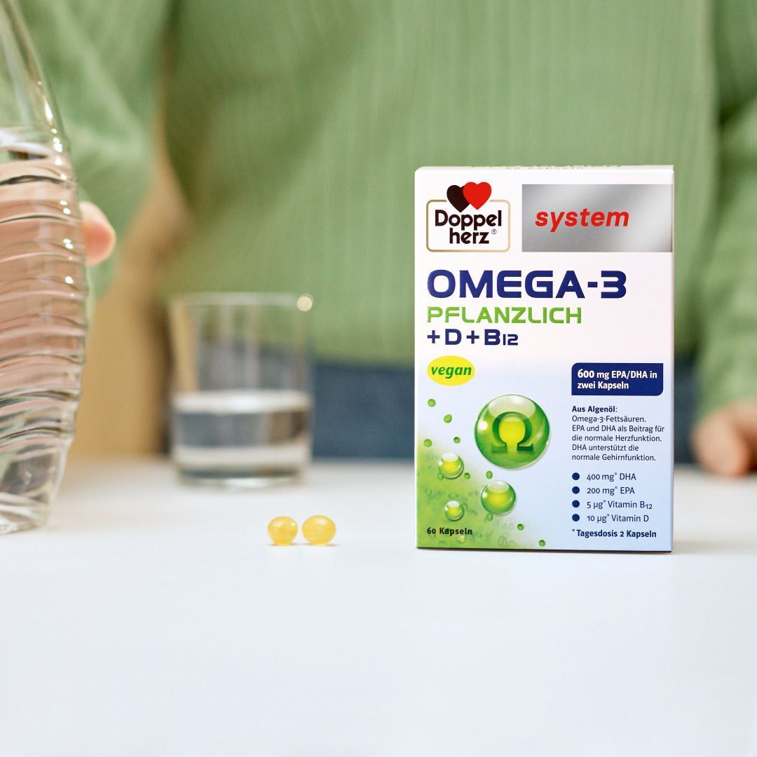 Packung Doppelherz Omega-3 pflanzlich neben Wasserflasche und Glas. Zwei Kapseln.