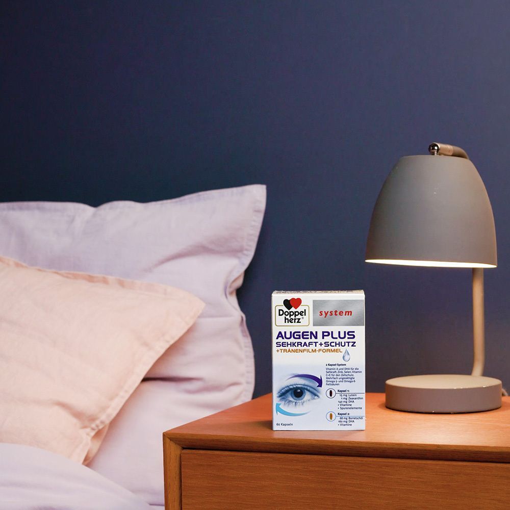 Doppelherz® system AUGEN PLUS SEHKRAFT + SCHUTZ-Packung auf einem Nachttisch. Neben einer Lampe und einem Kissen.
