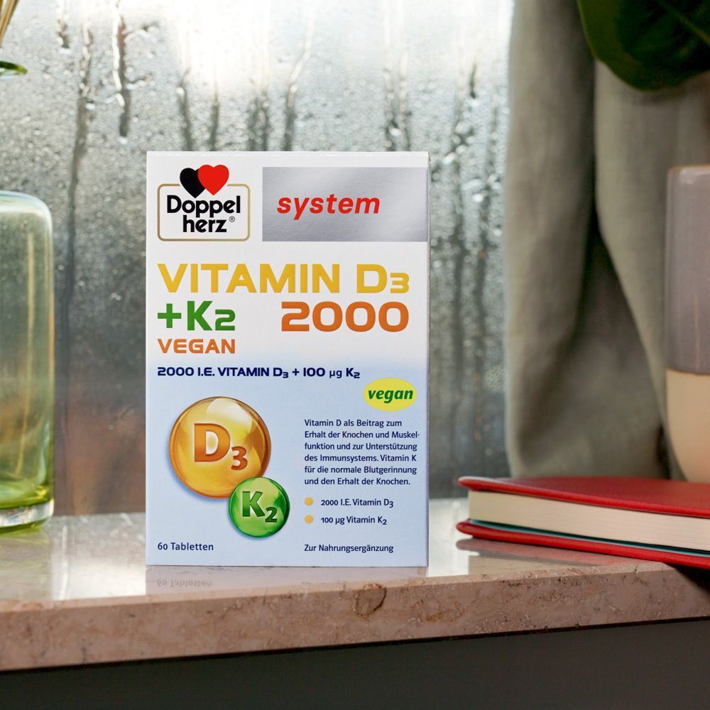 DOPPELHERZ Vitamin D3 + K2 2000 Tabletten-Packung. Weiße Verpackung mit Logo, Produktnamen und vegan-Hinweis. Auf einer Theke.