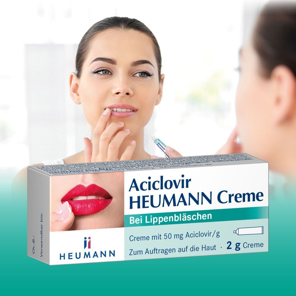 Frau trägt Creme auf Lippen auf. Im Hintergrund Schachtel Aciclovir Heumann Creme. Aufdruck: Bei Lippenbläschen. Heumann Logo.