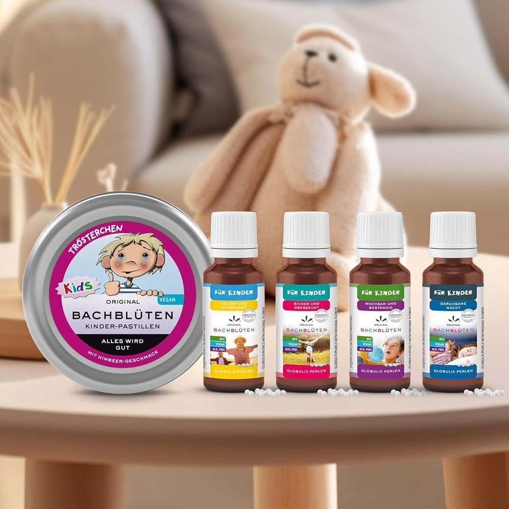 Runde Dose und vier Flaschen. Aufschrift: Kids Bachblüten. Flaschen mit Etiketten: Für Kinder, Bachblüten. Auf Tisch, neben Spielzeug.