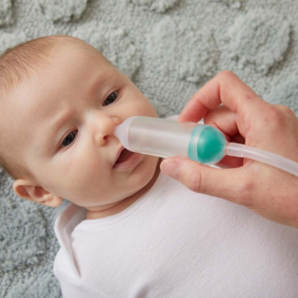 Ein Baby erhält einen Nasensauger. Der Sauger hat einen transparenten Behälter und eine grüne Spitze.