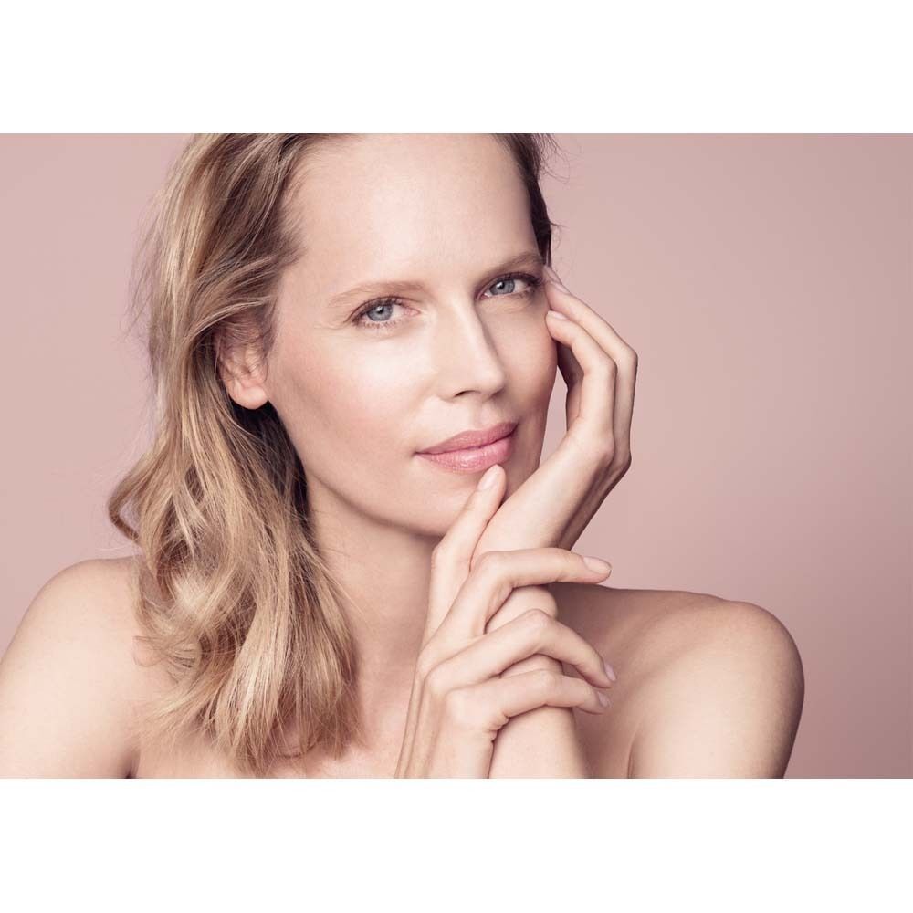 Porträt einer Frau mit blonden Haaren. Sie berührt sanft ihr Gesicht. Rosa Hintergrund.