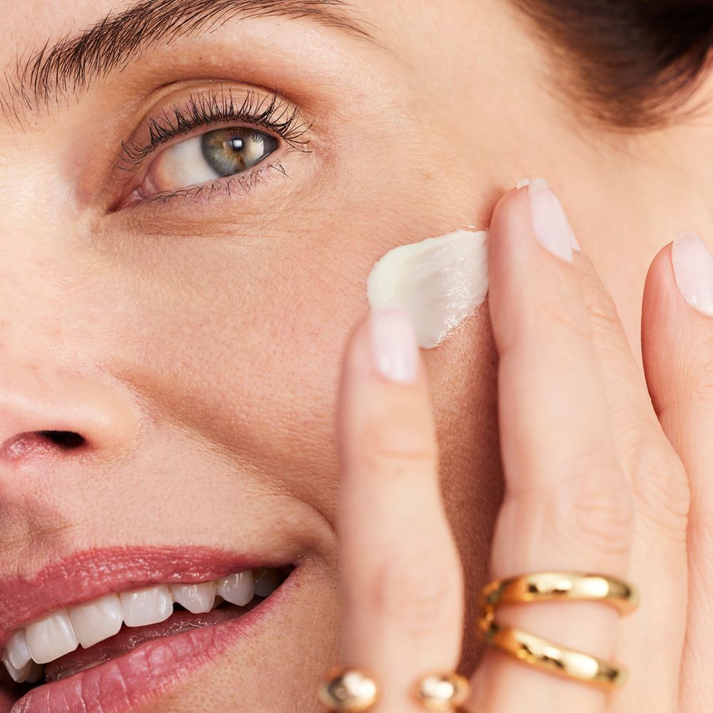 Frau trägt Creme auf. Creme auf Finger. Goldene Ringe. Hautpflege. Nahaufnahme.