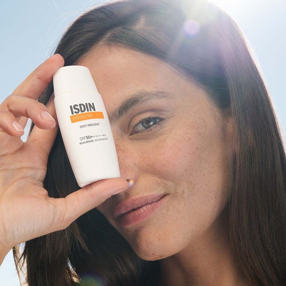 Frau hält eine weiße Flasche ISDIN FotoUltra Spot Prevent Fusion Fluid 2x. Orangefarbener Streifen mit Text.