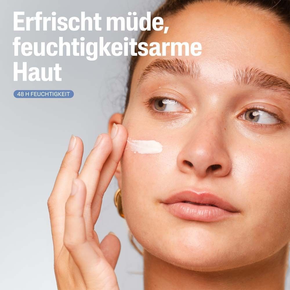Nahaufnahme einer Frau, die Creme auf ihr Gesicht aufträgt. Text: Erfrischt müde, feuchtigkeitsarme Haut.