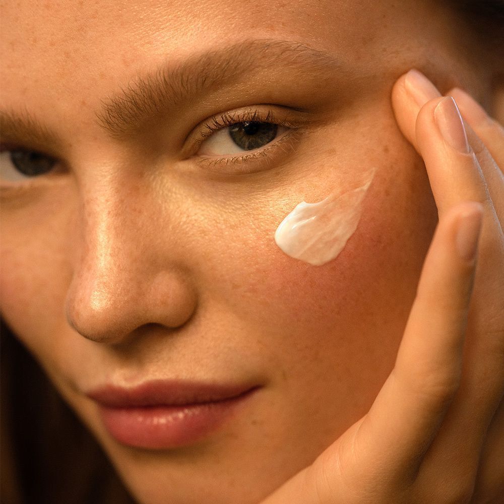 Nahaufnahme einer Frau, die Creme auf ihre Wange aufträgt. Creme ist sichtbar.