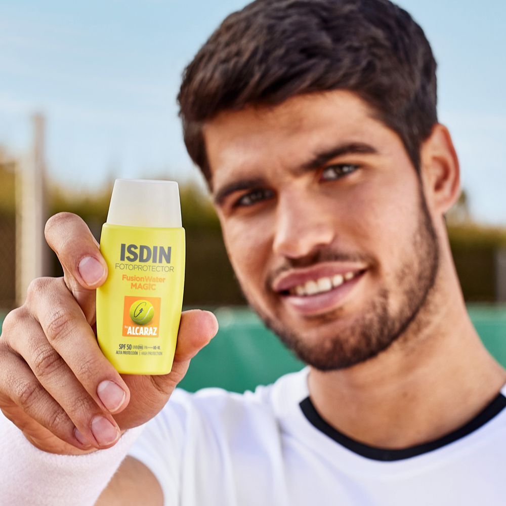 Ein Mann hält eine gelbe Flasche mit weißem Deckel. Aufschrift: ISDIN Fotoprotector Fusion Water Magic. Mit Alcaraz-Logo.