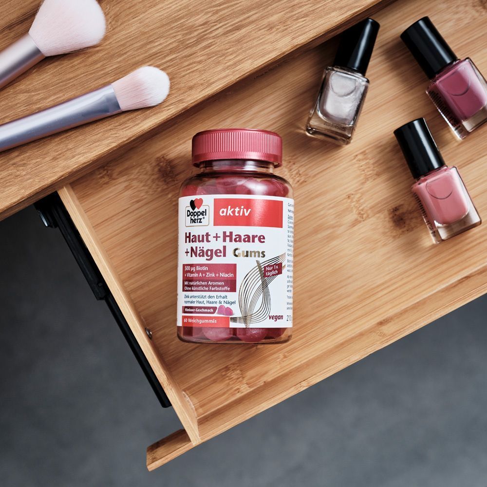 Flasche Doppelherz aktiv Haut + Haare + Nägel Gums auf Holzschublade. Pinsel und Nagellack daneben.