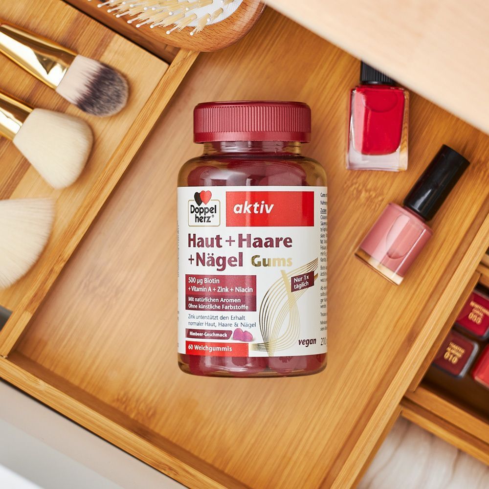 Flasche Doppelherz aktiv Haut + Haare + Nägel Gums auf Holzschublade. Nagellack und Pinsel daneben.