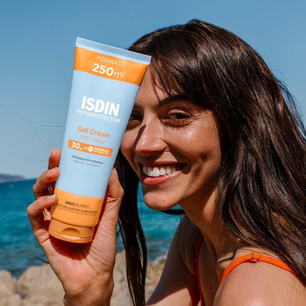 Frau hält eine Tube ISDIN Fotoprotector Gel Cream LSF 30. Sie lächelt. Hintergrund: Meer und Himmel.