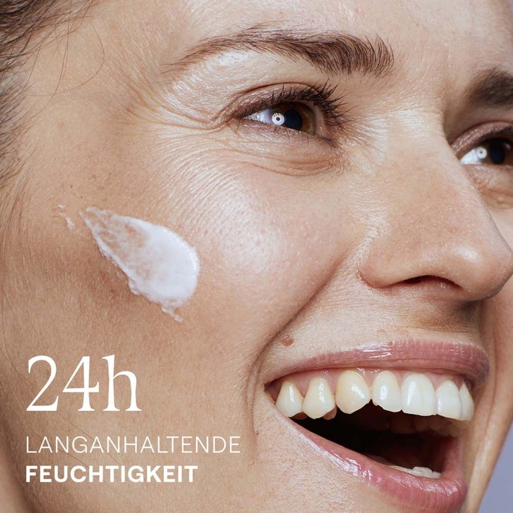 Nahaufnahme eines lächelnden Gesichts mit Creme auf der Haut. Text: 24h langanhaltende Feuchtigkeit.