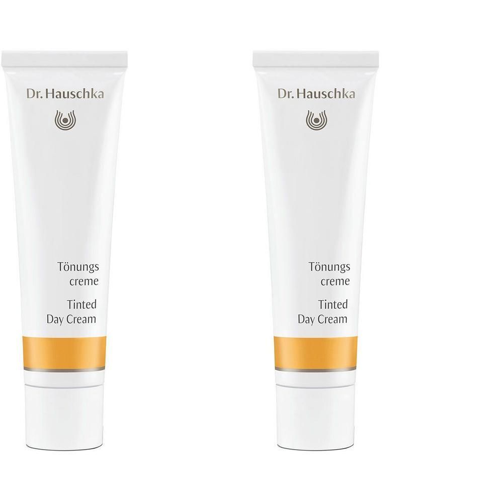 Zwei weiße Tuben Dr. Hauschka Getönte Creme mit orangefarbenem Band.