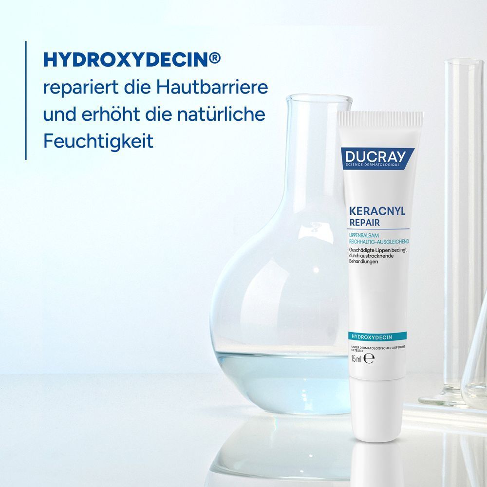 Eine Tube Lippenbalsam neben einem Laborgefäß. Aufschrift: DUCRAY, KERACNYL REPAIR, Lippenbalsam, 15 ml. Text: HYDROXYDECIN®.