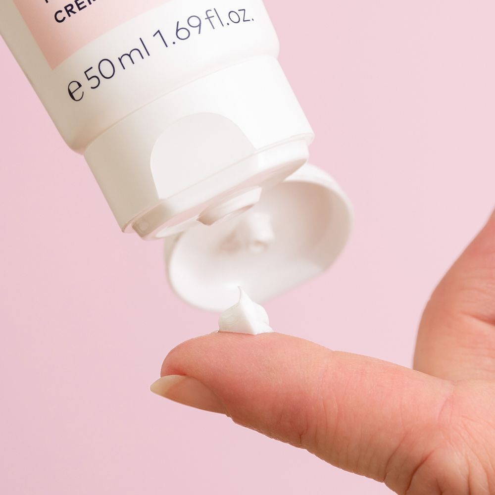 Eine kleine Menge weißer Creme wird aus einer Tube auf einen Finger gedrückt.