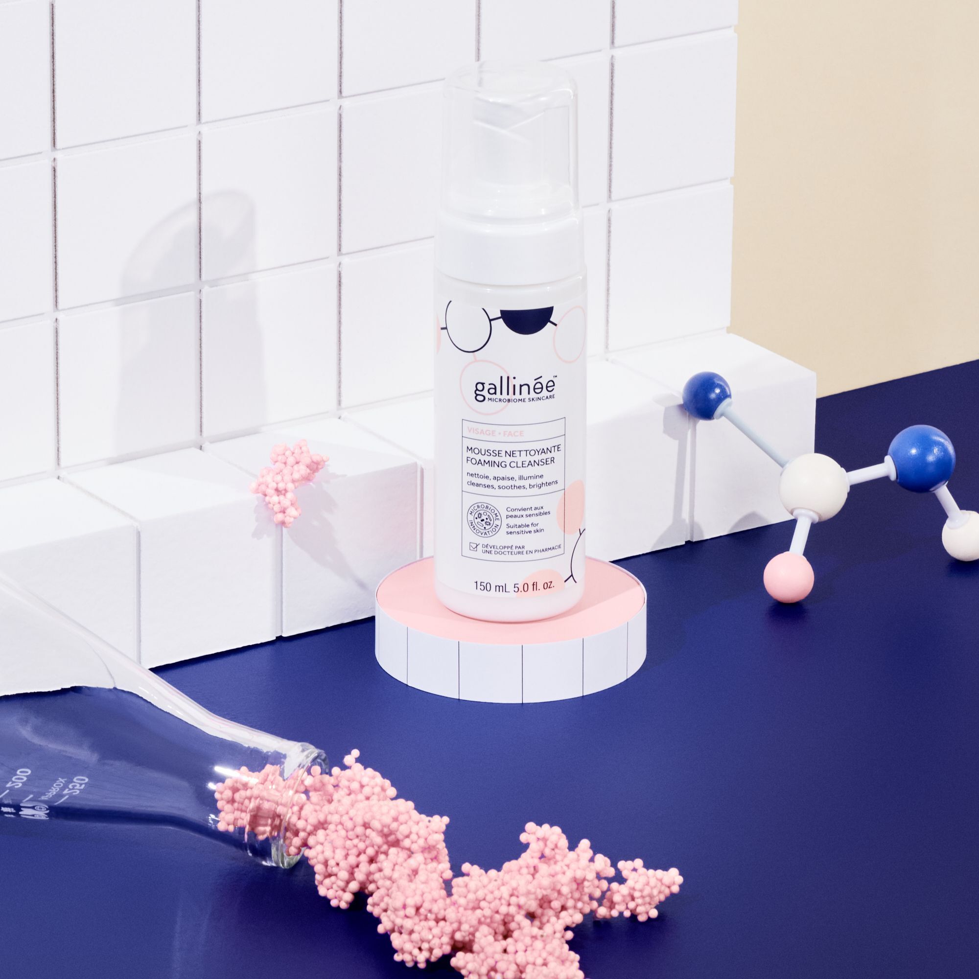 Eine weiße Flasche mit Pumpverschluss steht auf einem rosa Podest. Aufschrift: gallinée, MOUSSE NETTOYANTE FOAMING CLEANSER. 150 ml. Dekoration.