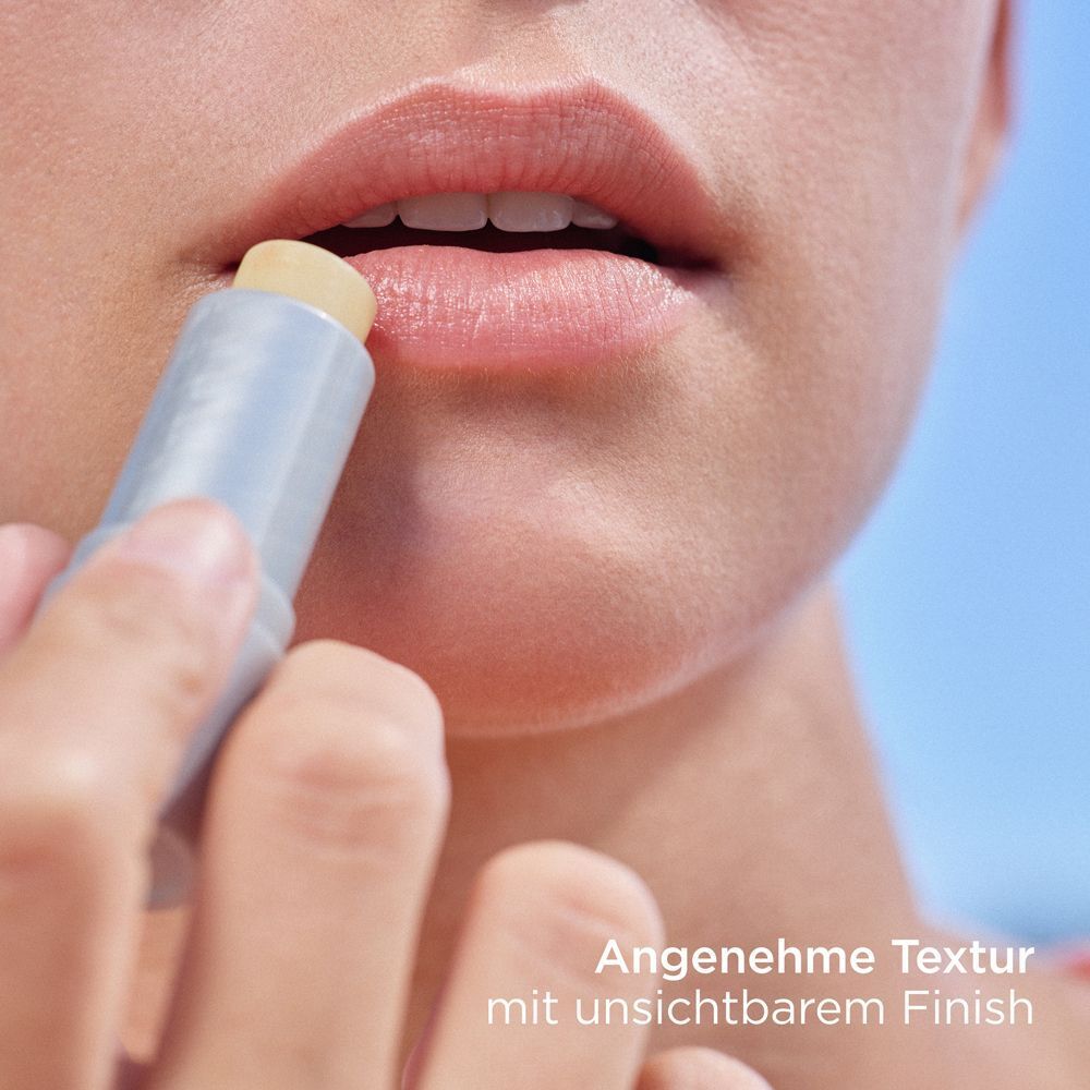 Lippen werden mit einem Lippenbalsam-Stift eingerieben. Der Stift hat eine weiß-silberne Hülle mit orangefarbener Schrift.
