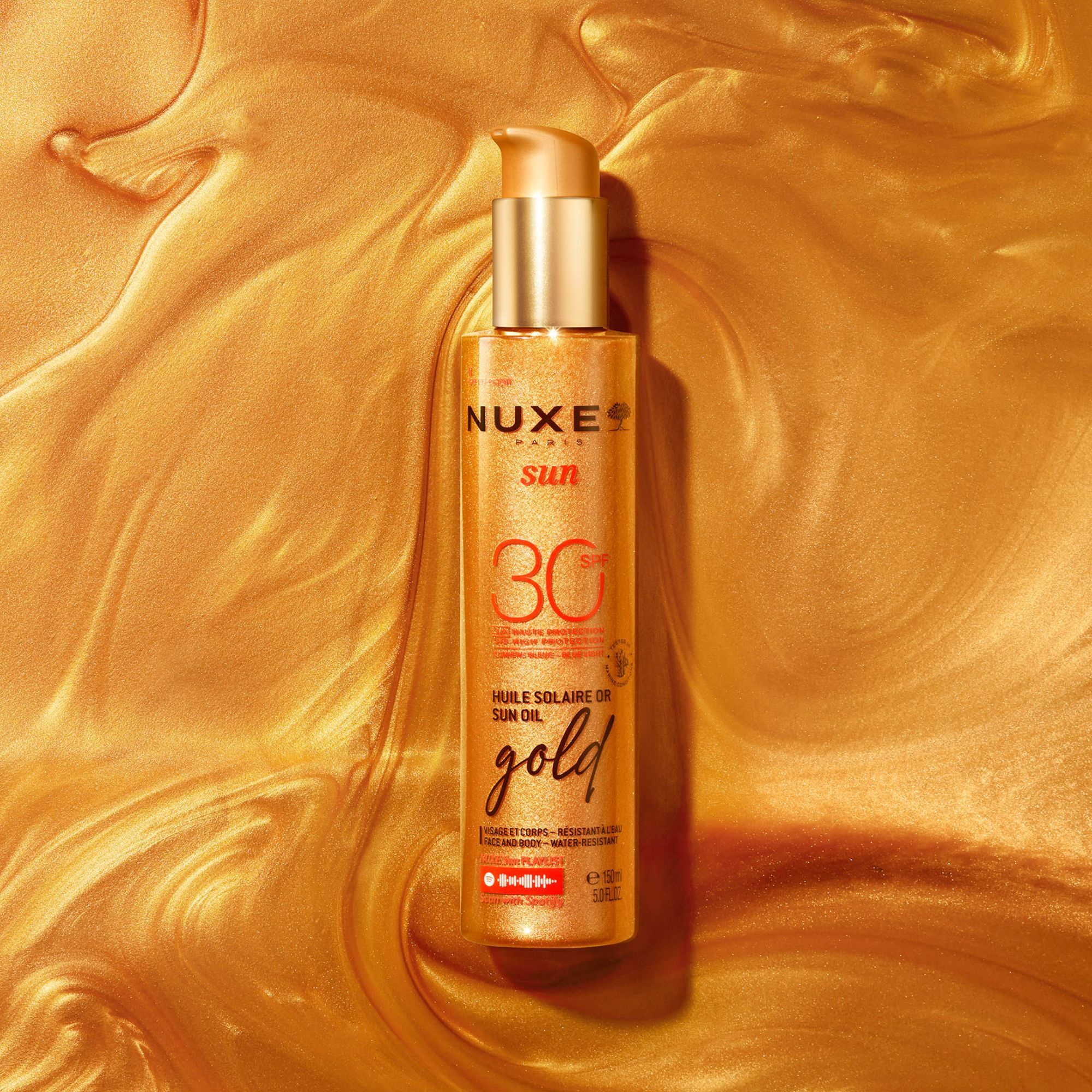 Goldfarbene Flüssigkeit mit einer Flasche NUXE Sun Sonnenöl LSF 30. Aufschrift: Huile Solaire Or, gold.