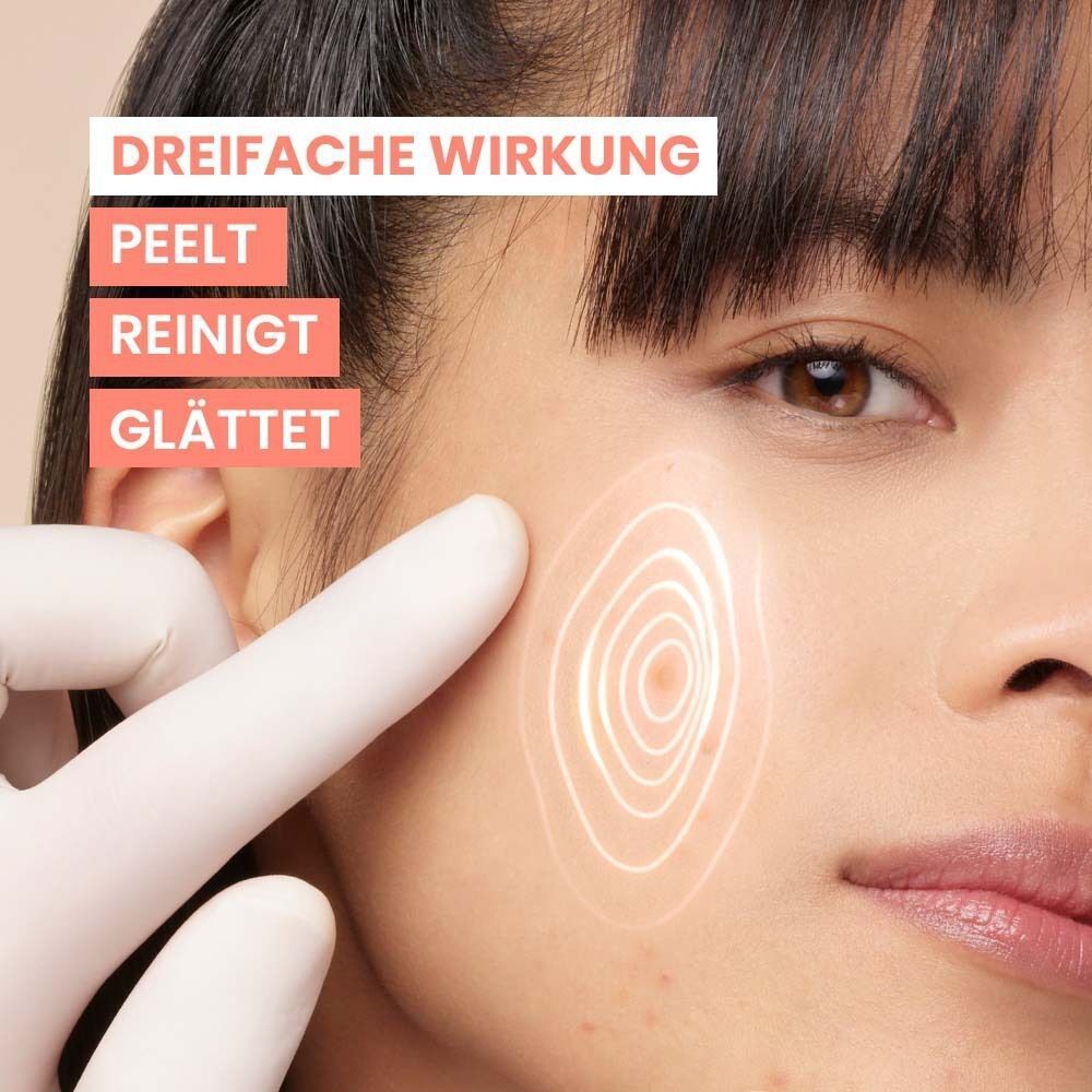 Gesicht einer Frau. Ein Finger berührt die Haut. Text: Dreifache Wirkung: Peelt, Reinigt, Glättet. Hintergrund: hell.