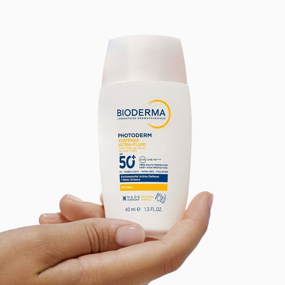 Weiße Flasche in einer Hand gehalten. Aufschrift: BIODERMA Photoderm Xdefense Ultra-Fluid LSF 50+.