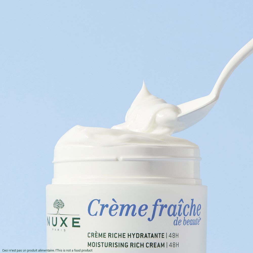 Weißes Creme Produkt in einem Tiegel. Ein weißer Löffel hebt Creme aus dem Tiegel.