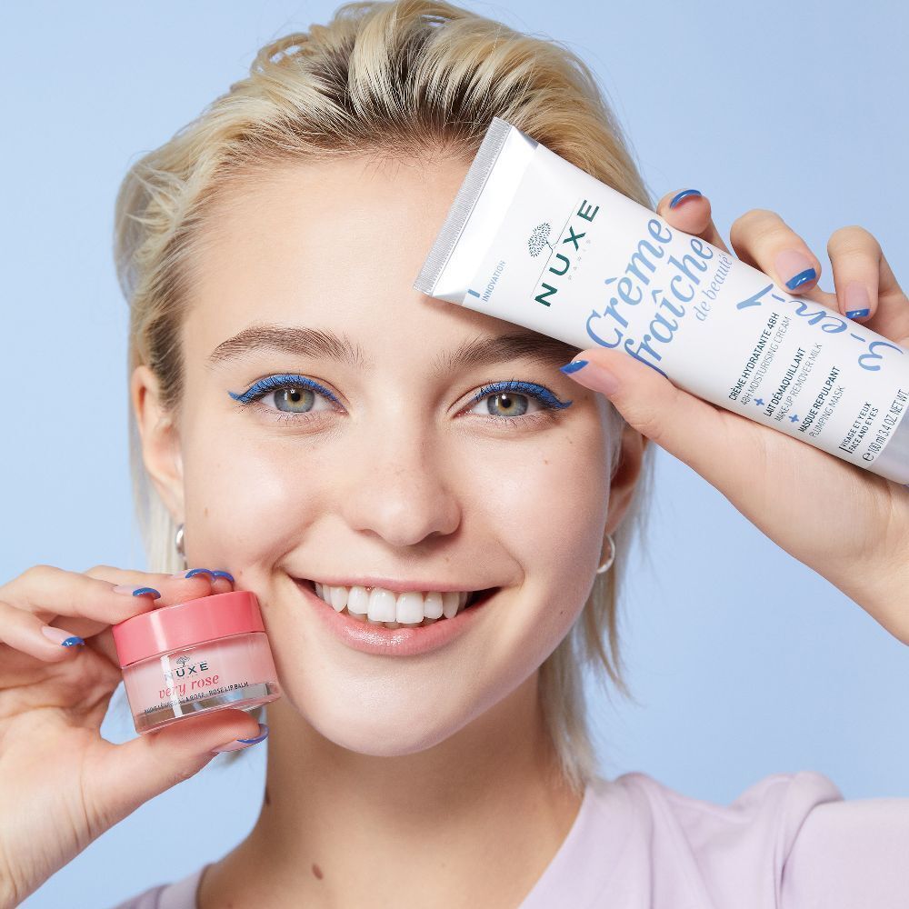 Frau hält NUXE Produkte: Tube Crème Fraîche, Lippenbalsam und ein weiteres Produkt.