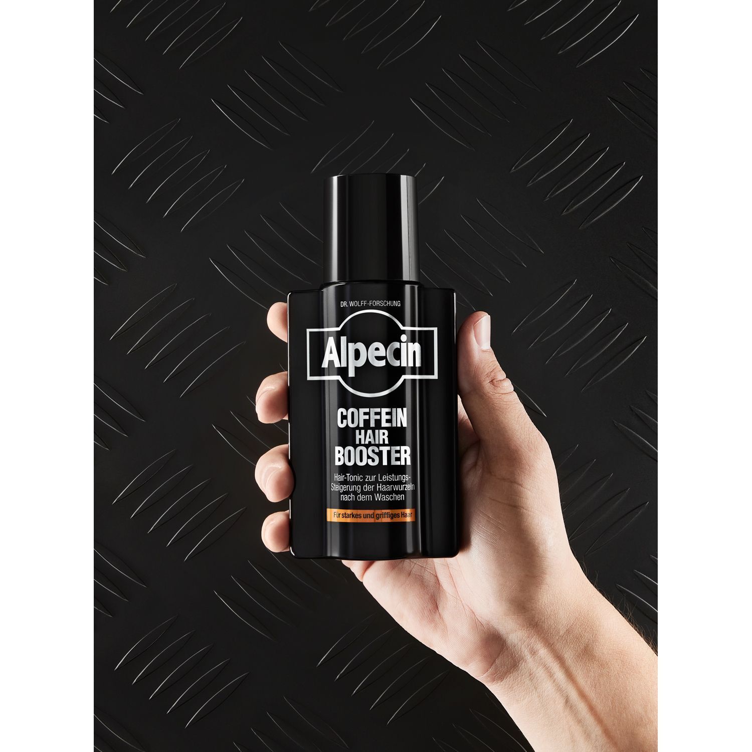 Hand hält eine schwarze Flasche. Aufschrift: Alpecin Coffein Hair Booster.