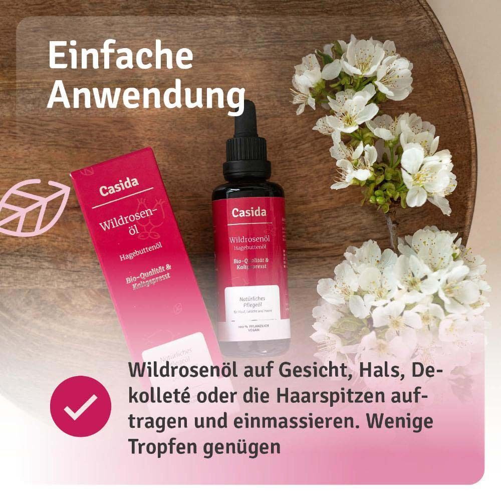 Flasche Wildrosenöl mit Verpackung und Text. Anwendung: Auf Gesicht, Hals, Dekolleté oder Haarspitzen auftragen. Wenige Tropfen.