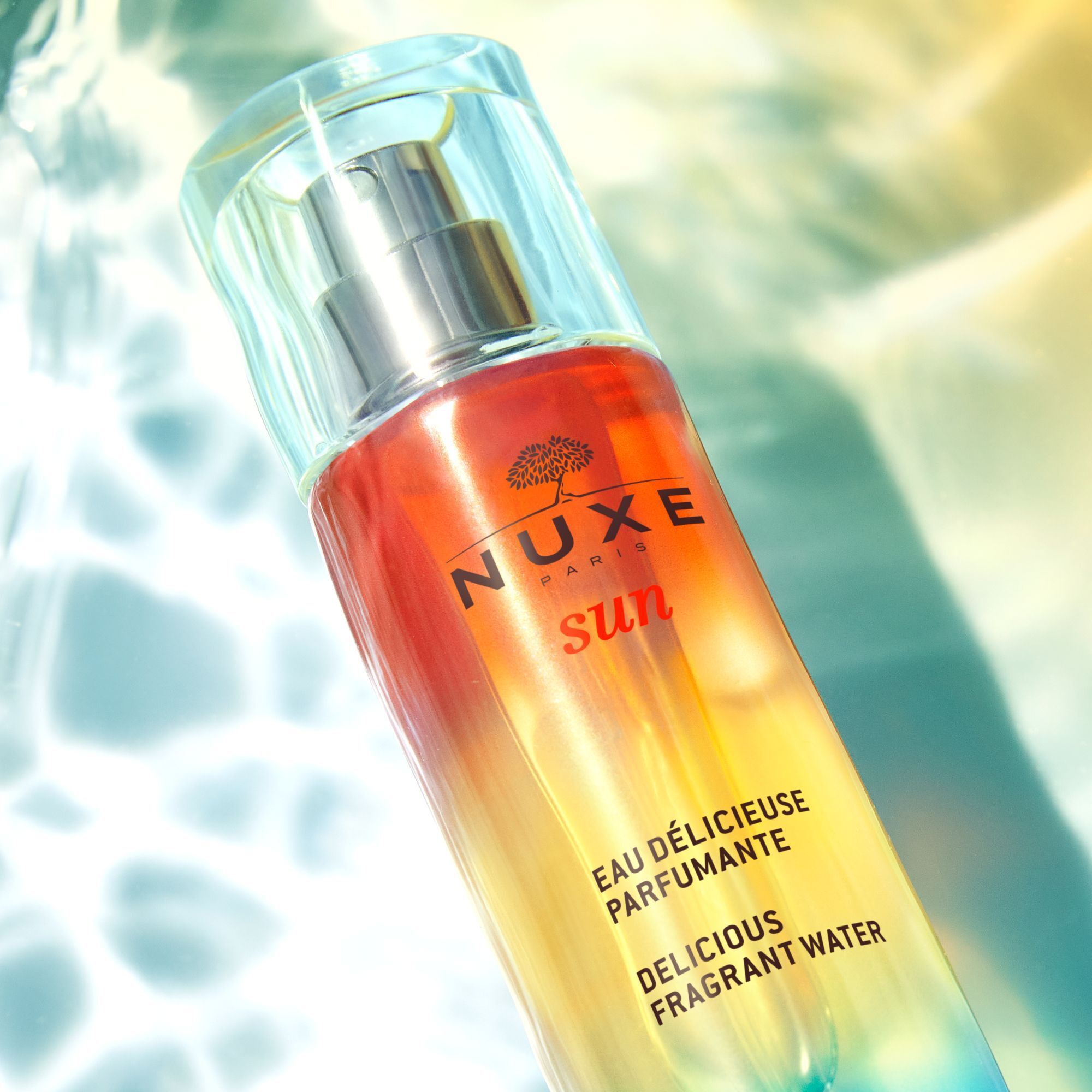 Flakon mit Sprühkopf. Farbverlauf von Blau nach Gelb und Orange. Aufschrift: NUXE Sun, Eau Délicieuse Parfumante, Delicious Fragrant Water.