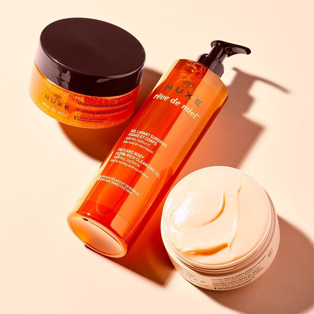 Drei NUXE Produkte: Duschgel, Creme und Honig-Peeling. Orange, weiß und braun. Auf hellem Hintergrund.