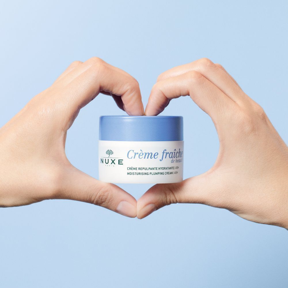 Ein Tiegel Crème fraîche de Beauté, gehalten von zwei Händen in Herzform. Aufschrift: NUXE Paris, Crème fraîche de beauté.